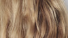 Close-up view of dry, frizzy blonde hair strands with visible rough texture, uneven fiber alignment, and signs of damage before restorative hair treatment.